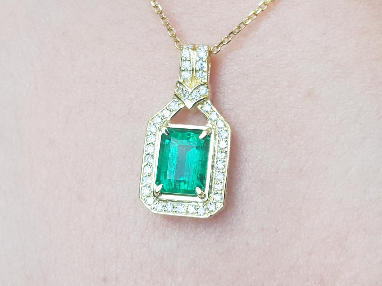 Natural colombian emerald pendant with diamond accents on a gold chain against a pink skin background