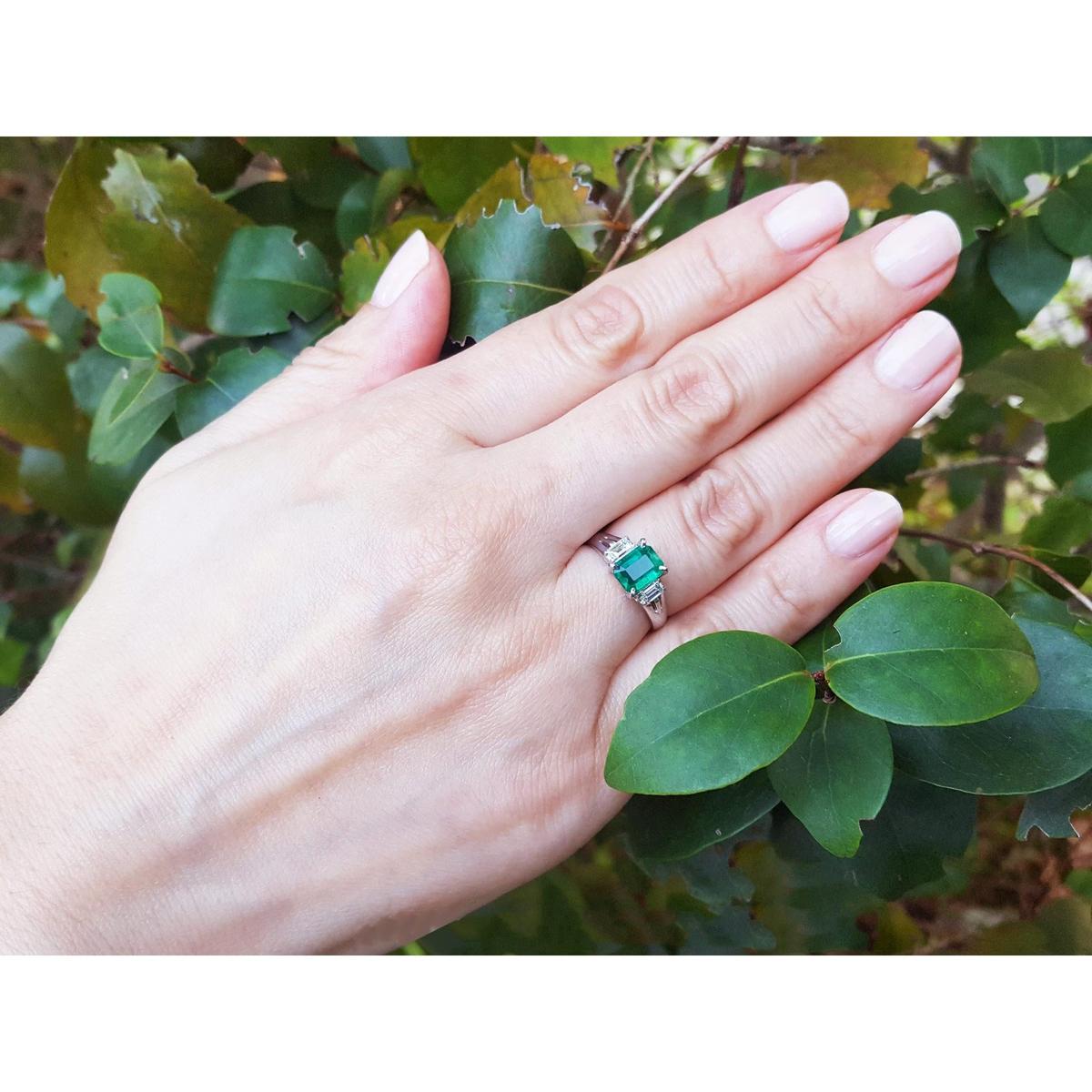 Hand wearing an emerald platinum ring with a leafy background.