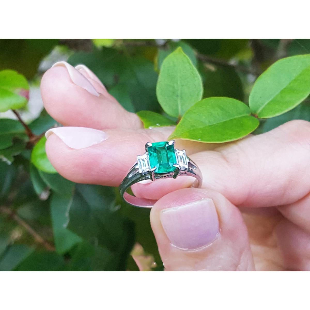 Natural emerald platinum ring held between fingers with a green leafy background