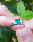 Natural emerald platinum ring held between fingers with a green leafy background