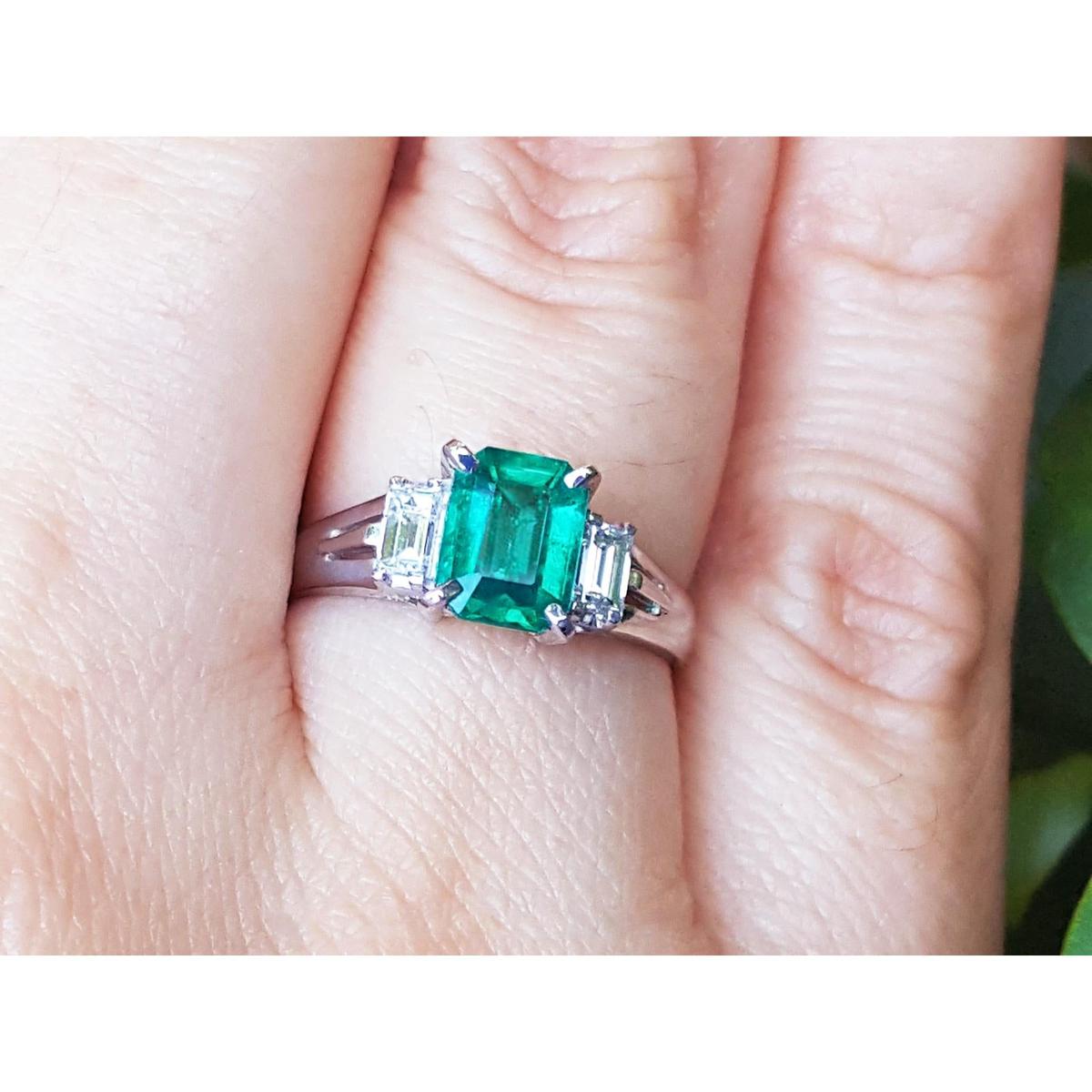 Emerald and side diamonds platinum ring on a hand.