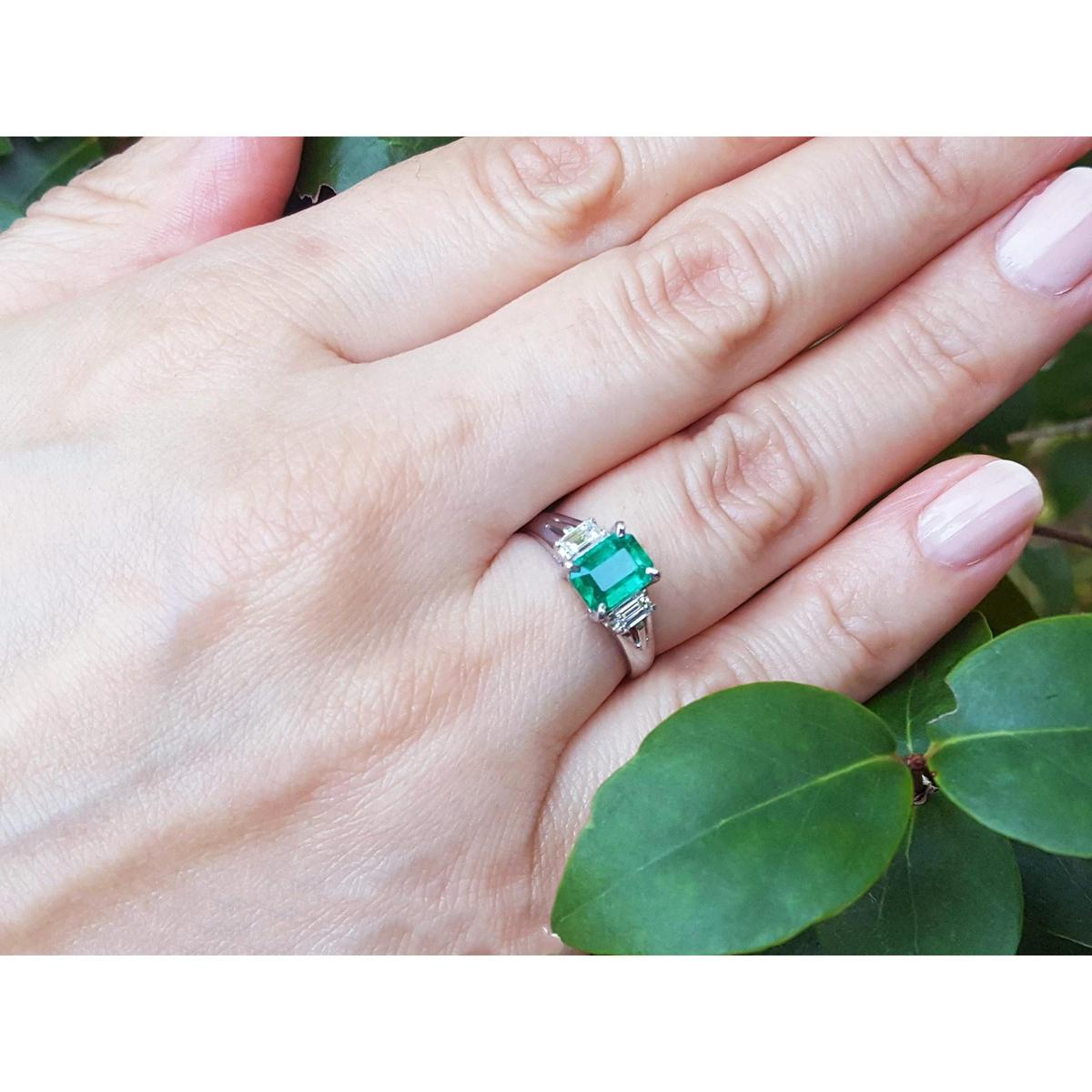 Hand wearing a brides emerald platinum ring with a leafy background.