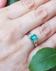 Hand wearing a brides emerald platinum ring with a leafy background.