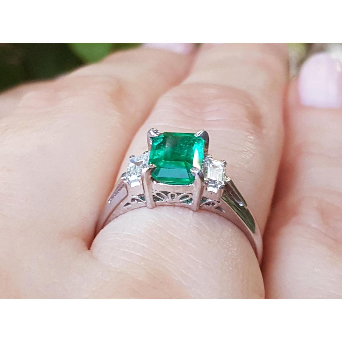 Emerald-cut emerald platinum ring held on a hand.