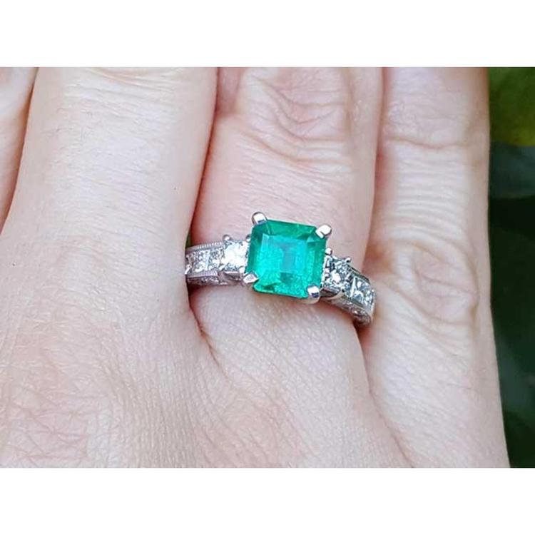Hand wearing a square emerald ring with side diamond princess cut in white gold.