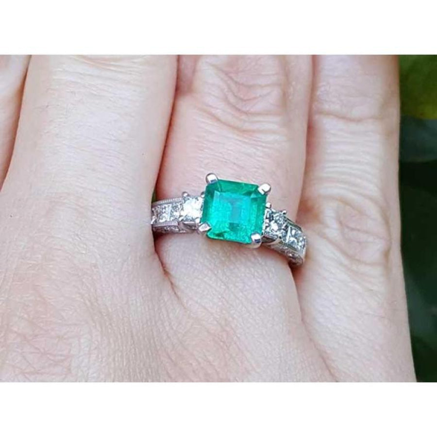 Hand wearing a square emerald ring with side diamond princess cut in white gold.