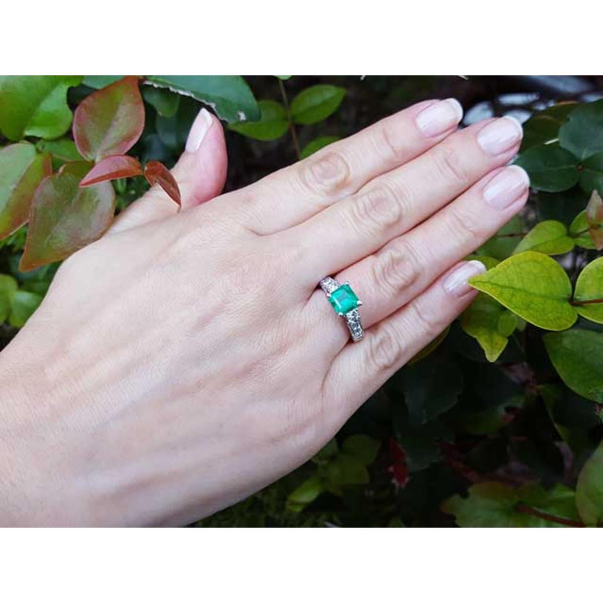 Hand wearing a natural Colombian emerald ring on a green leafy background.