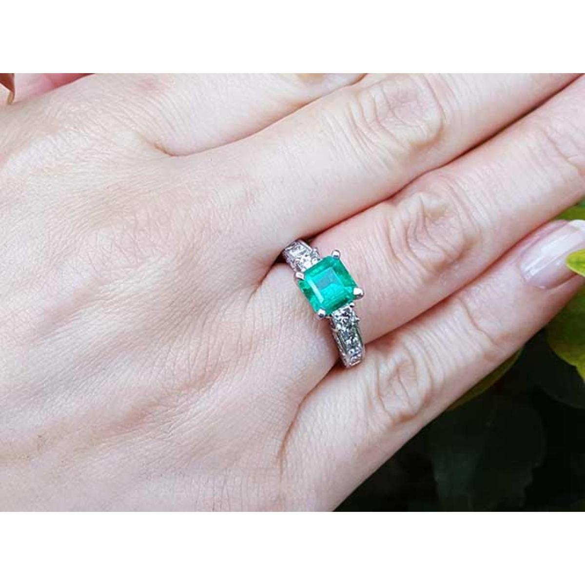 A woman's hand wearing an emerald and princess cut diamond engagement ring.