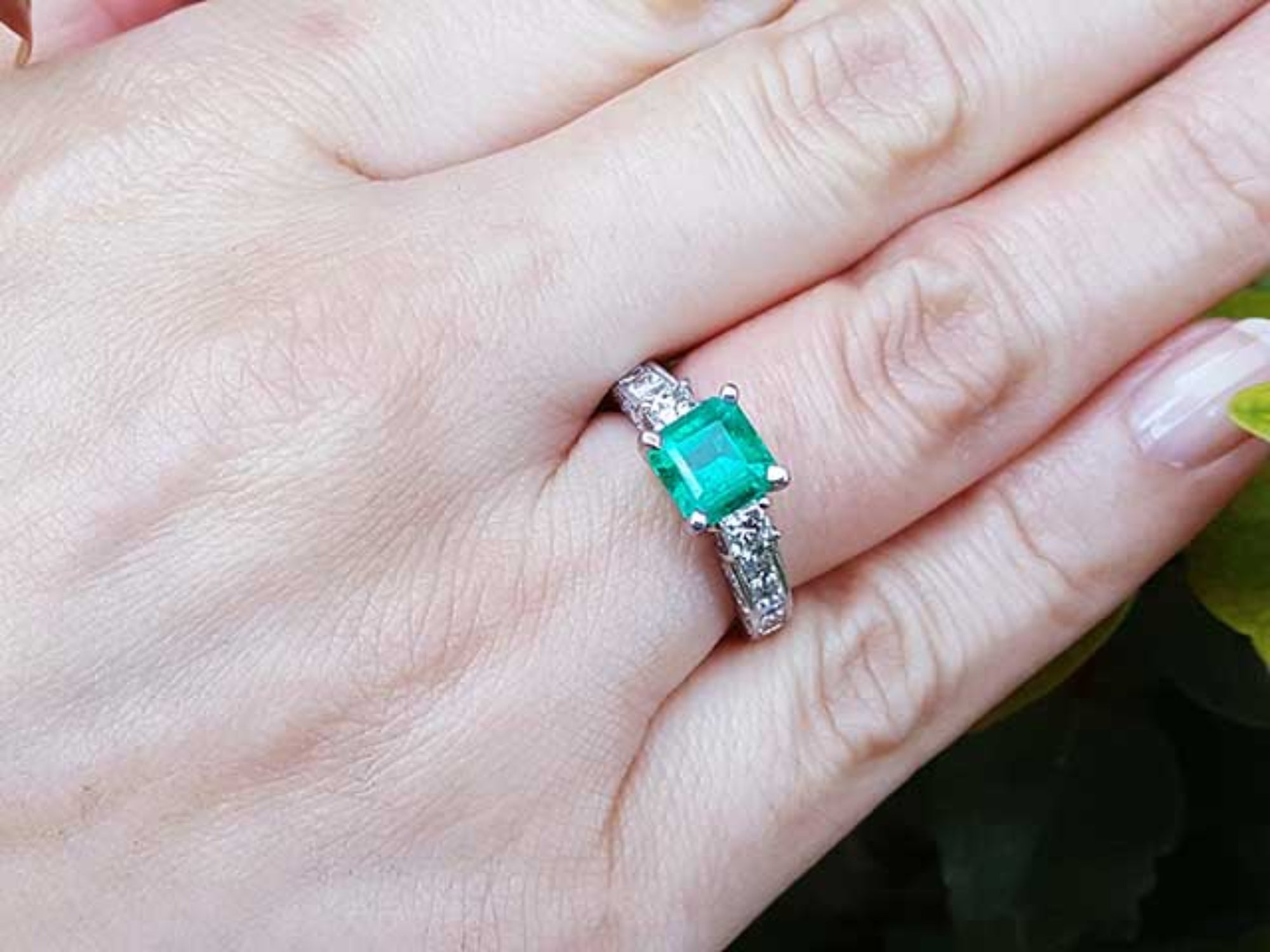 A woman&#39;s hand wearing an emerald and princess cut diamond engagement ring.