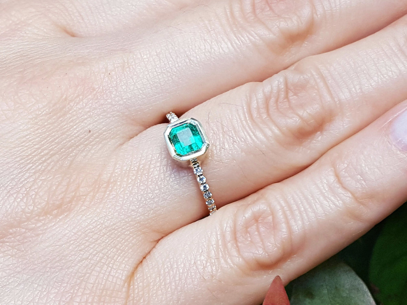 A square natural colombian emerald ring on a hand.