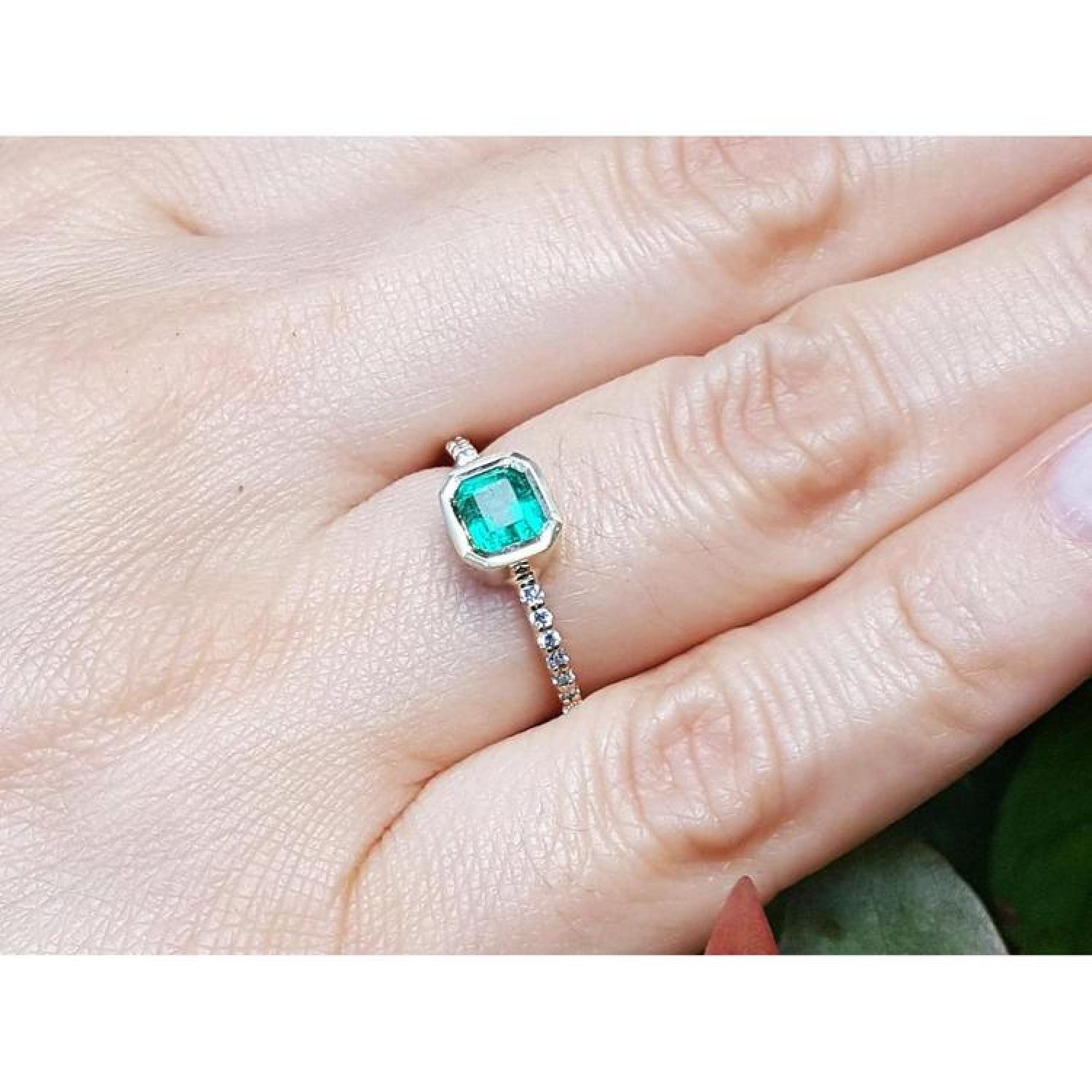14K yellow gold ring with a bezel-set emerald and accent diamonds on a woman's finger.