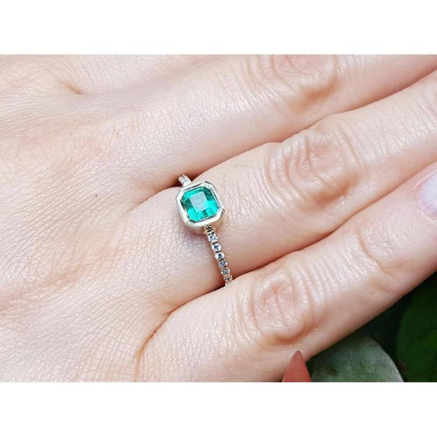 14K yellow gold ring with a bezel-set emerald and accent diamonds on a woman's finger.