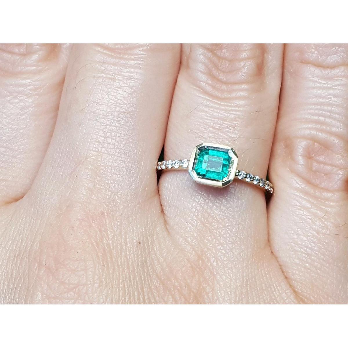 A bezel set natural colombian emerald ring with accent diamonds on a finger.