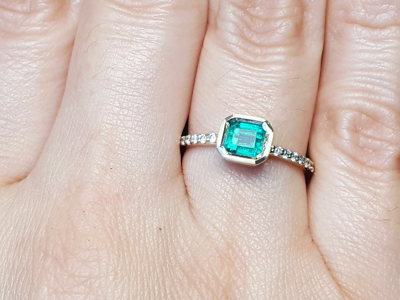 A bezel set natural colombian emerald ring with accent diamonds on a finger.