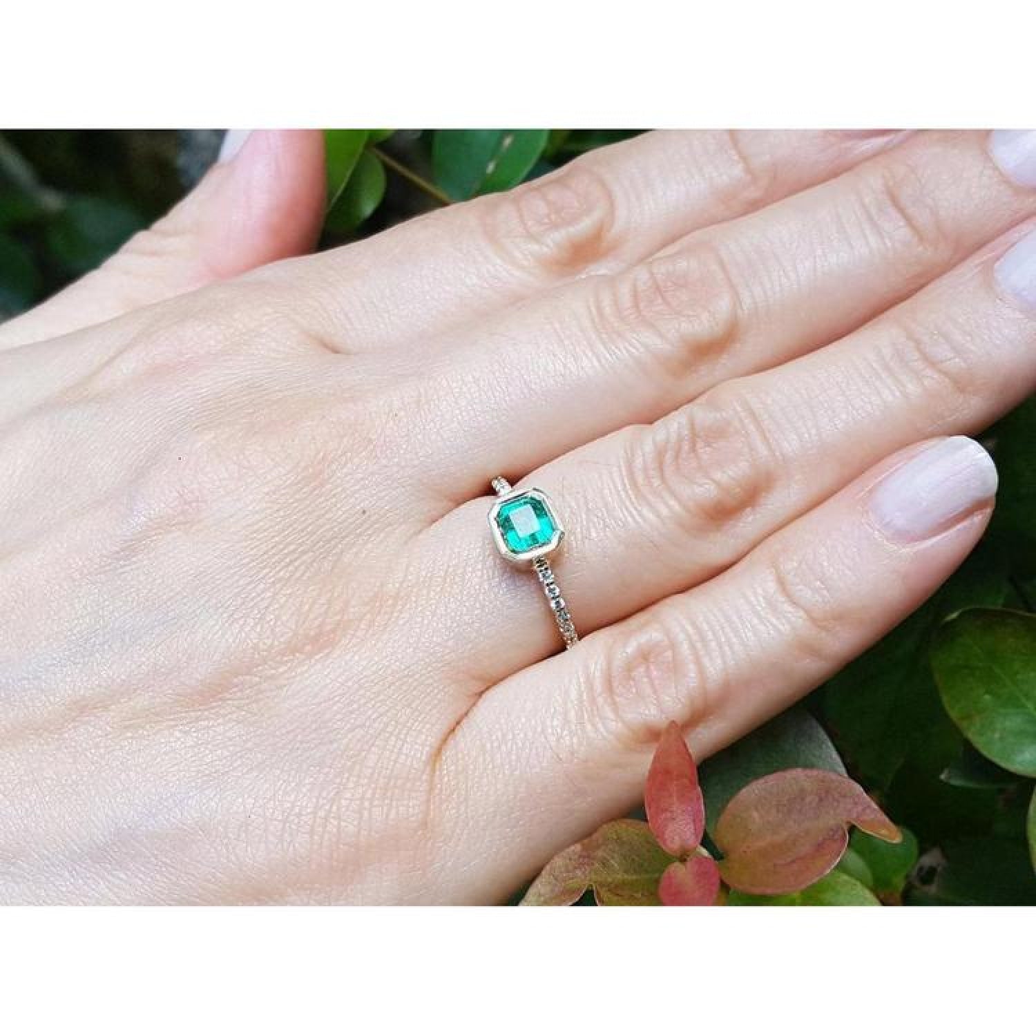 Bezel-set emerald ring with accent diamonds on a 14K yellow gold band, worn on a hand.