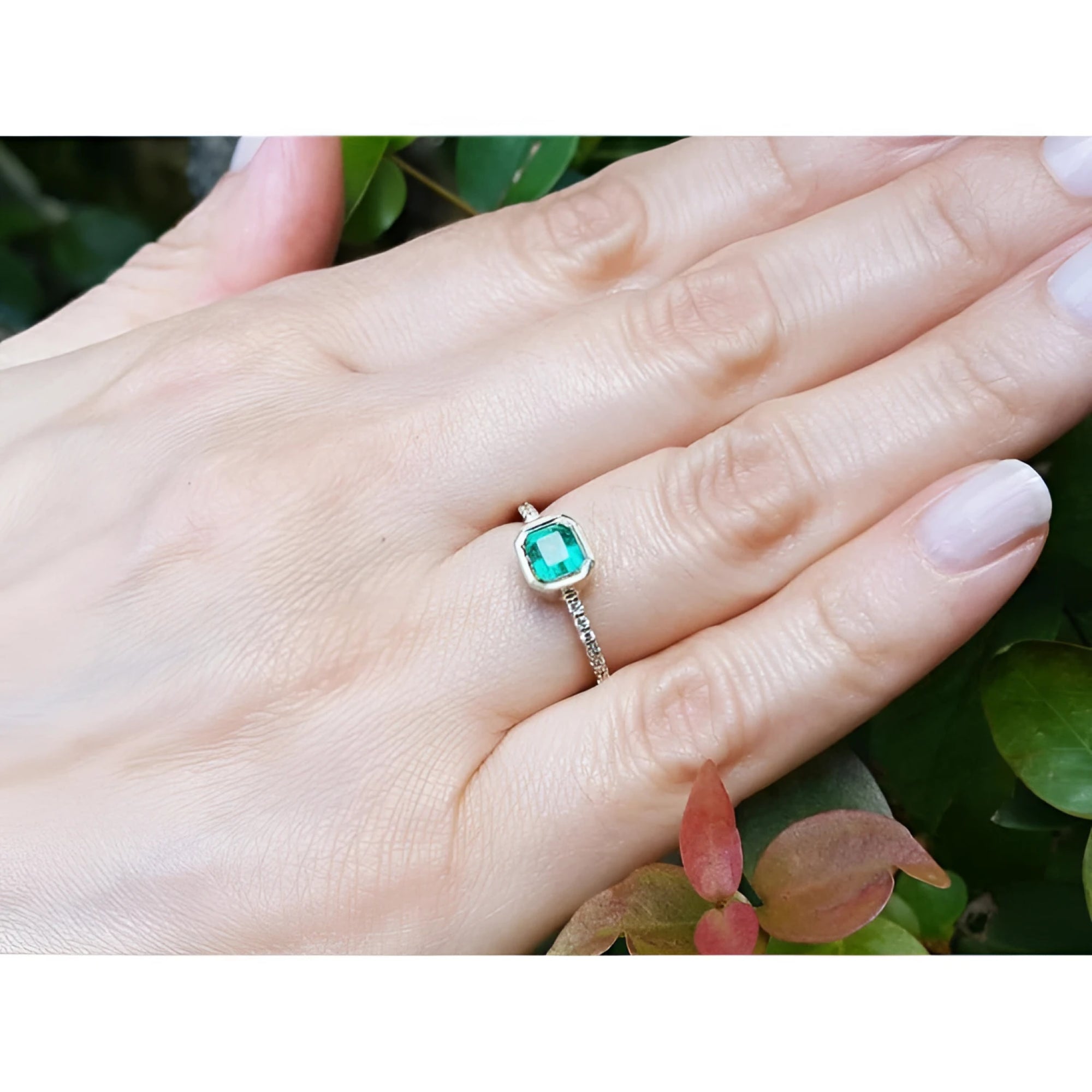 Bezel-set emerald ring with accent diamonds on a 14K yellow gold band, worn on a hand.