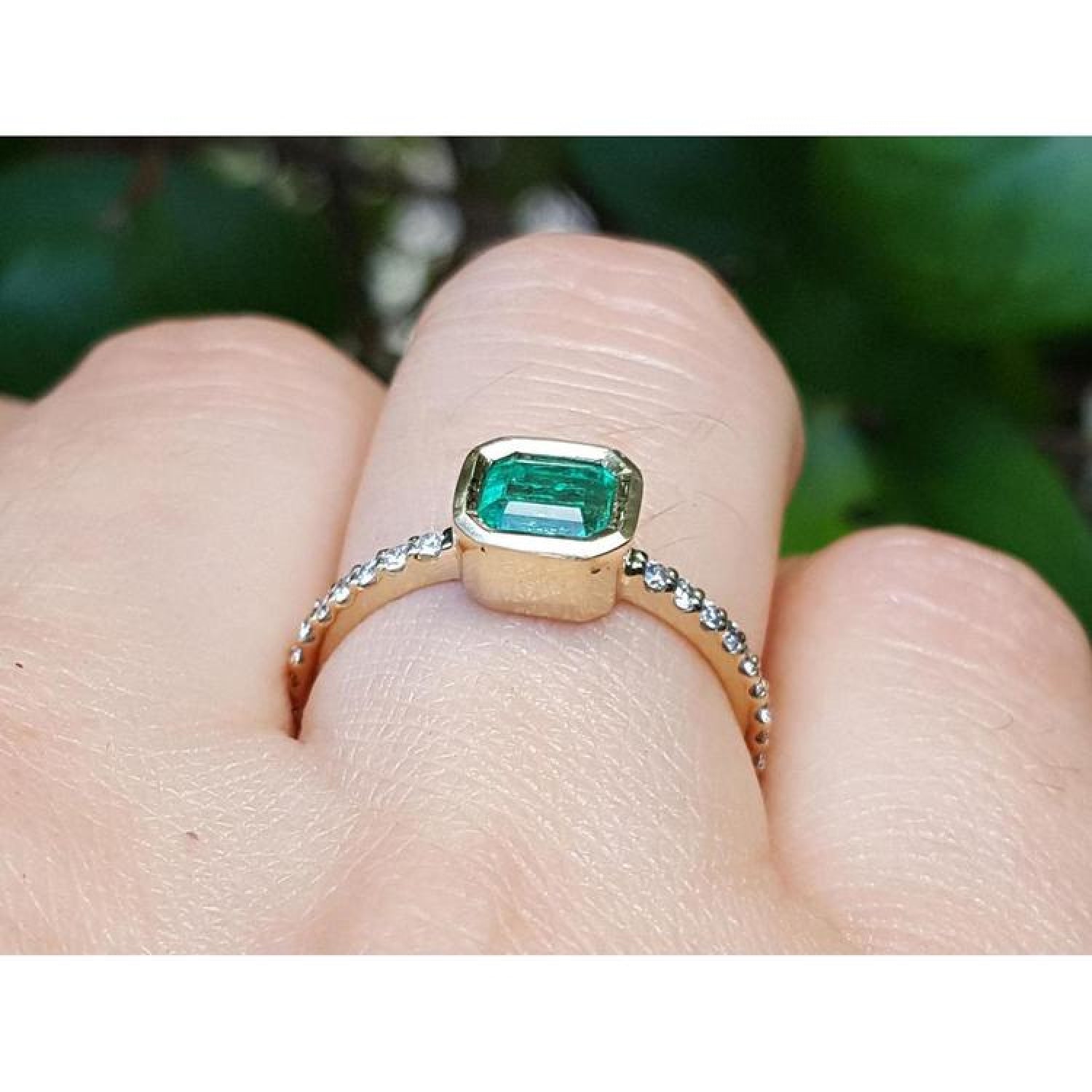 Bezel-set emerald ring with accent diamonds in 14K yellow gold, worn on a finger.