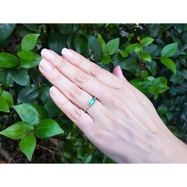 Hand wearing a Colombian emerald ring for mother's day with a leafy background.