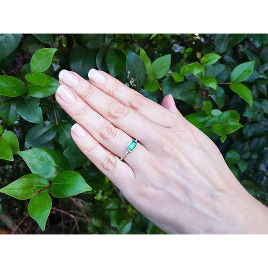 Hand wearing a 14K yellow gold east-west emerald-cut bezel set ring with accent diamonds.