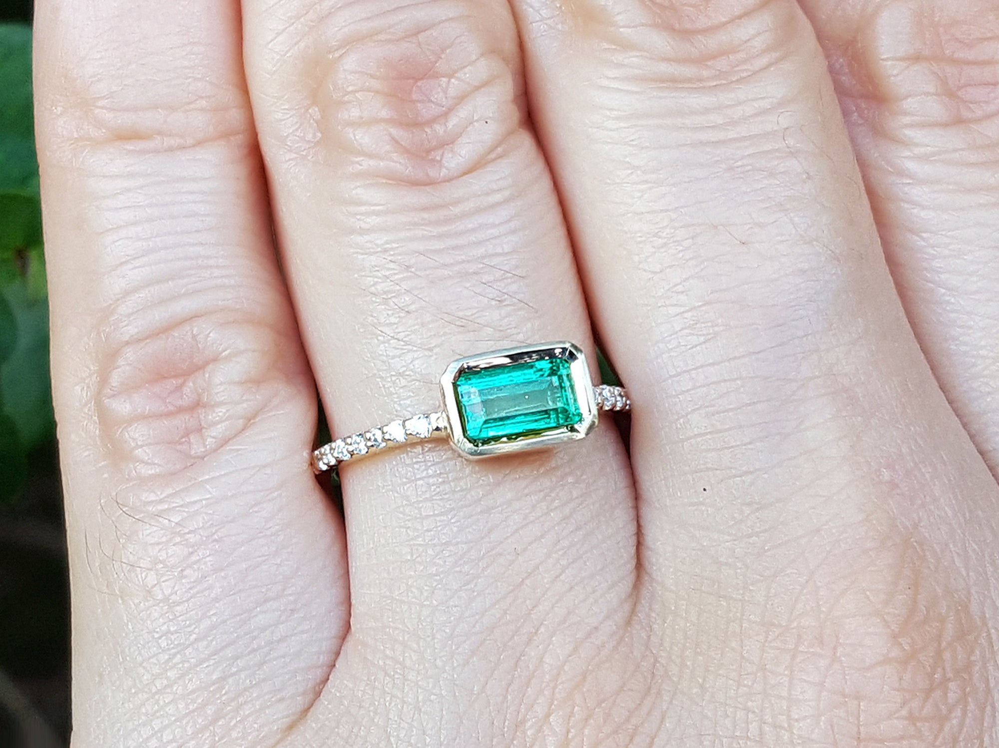 Emerald-cut gemstone ring on a finger with a blurred background