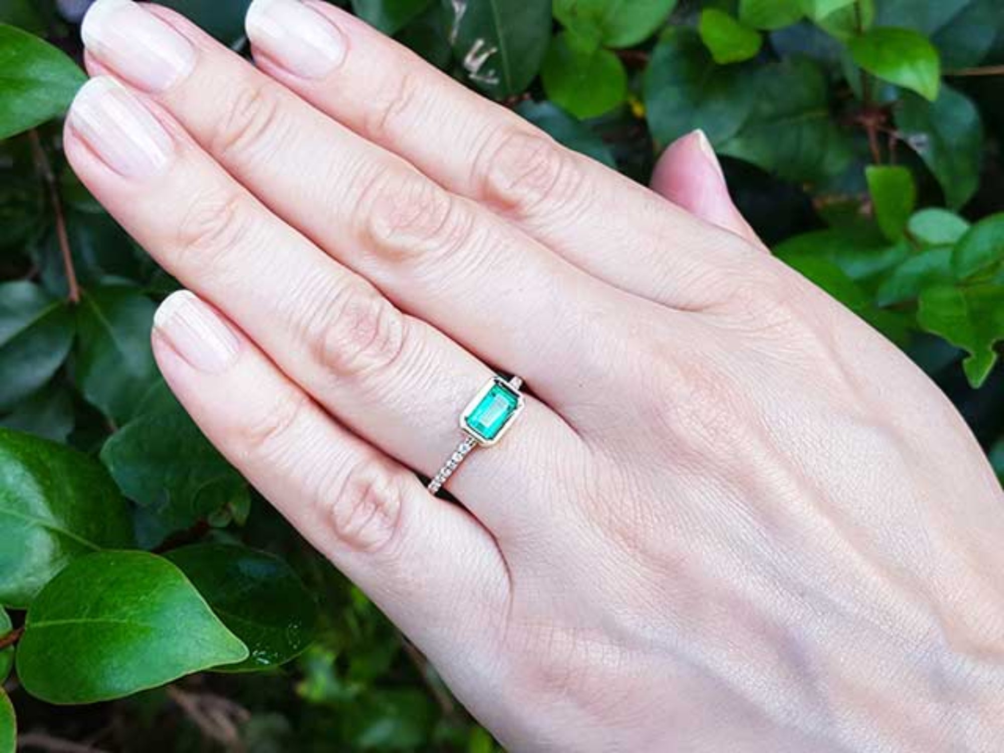 Hand wearing a mother’s day emerald ring the perfect gift for her with a leafy background.
