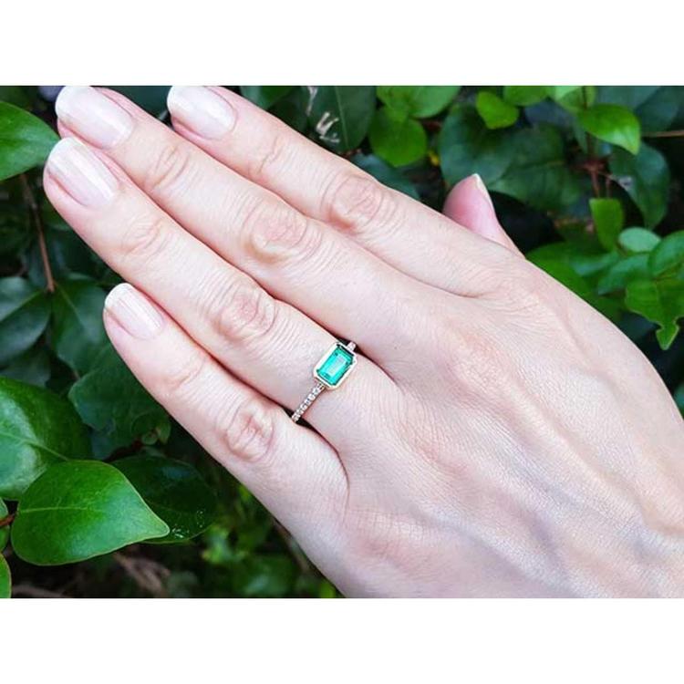 Hand wearing a mother’s day emerald ring the perfect gift for her with a leafy background.