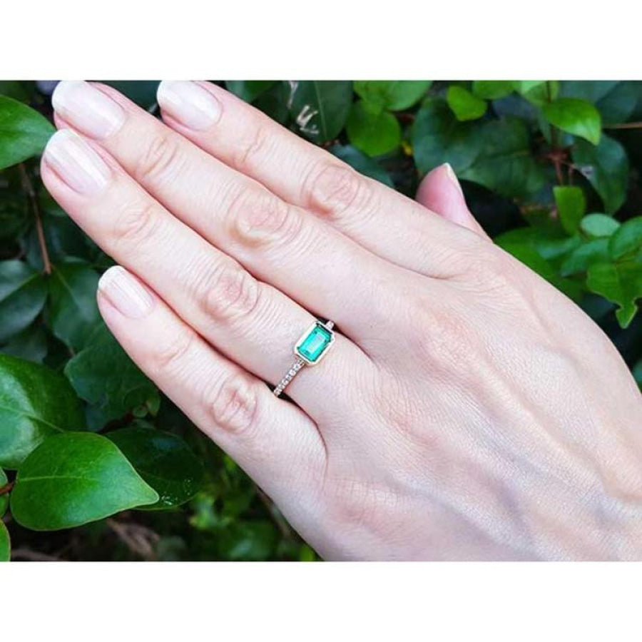 East-west emerald-cut Colombian emerald ring, bezel set in 14K yellow gold with diamond accents.