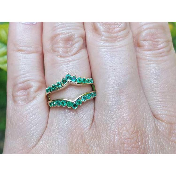 An emerald ring guard made of 14k yellow gold on a finger.