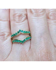 An emerald ring guard made of 14k yellow gold on a finger.