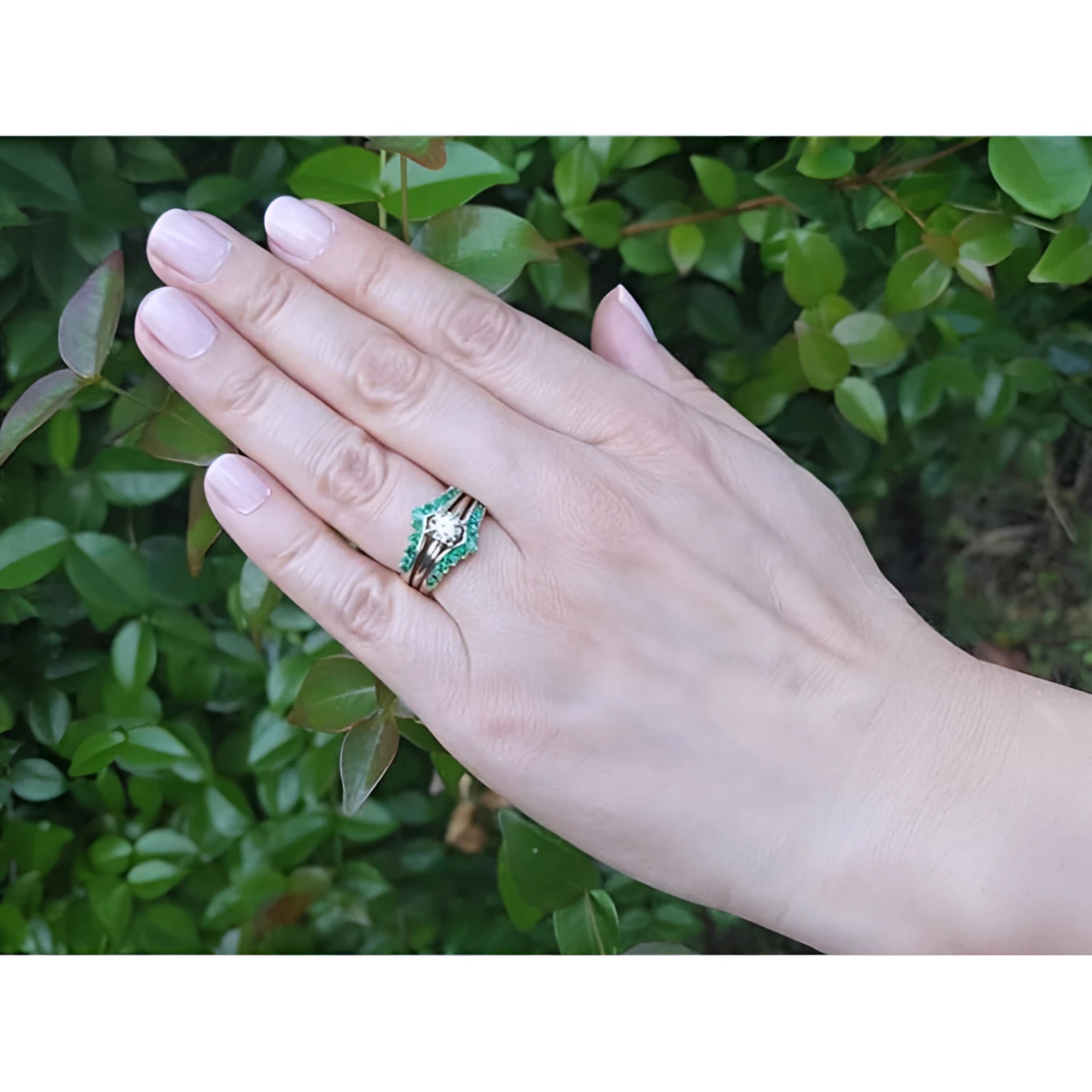 Hand wearing a 14K yellow gold emerald ring guard with a solitaire diamond ring, against green foliage.