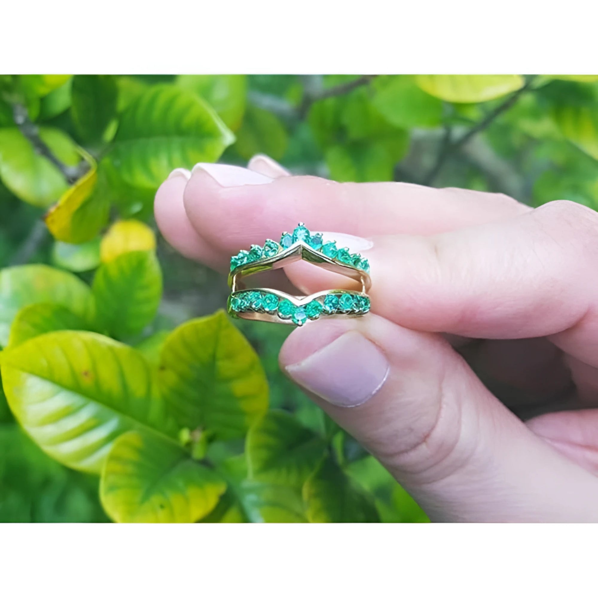 14K yellow gold emerald ring guard with 0.75 ct. round-cut Colombian emeralds, held against green leaves.