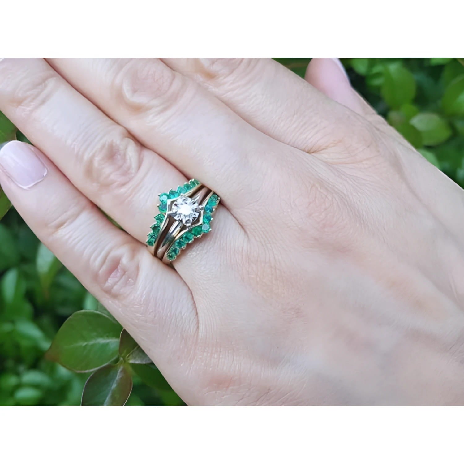 Hand wearing a 14K yellow gold emerald ring guard with a solitaire diamond ring, surrounded by green leaves.