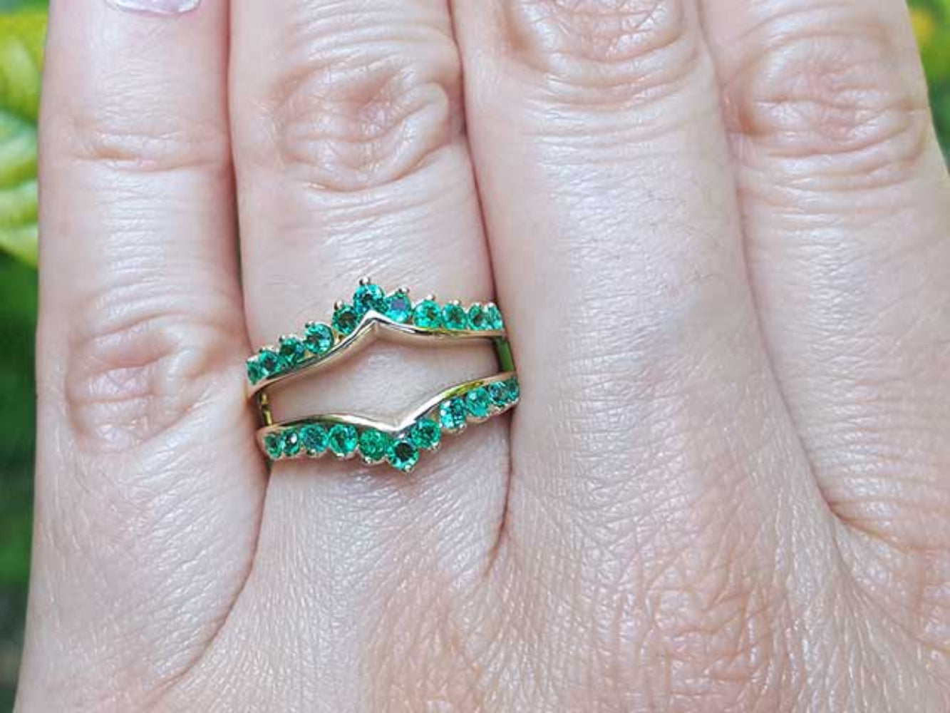 An emerald ring guard on a finger with a blurred green background.