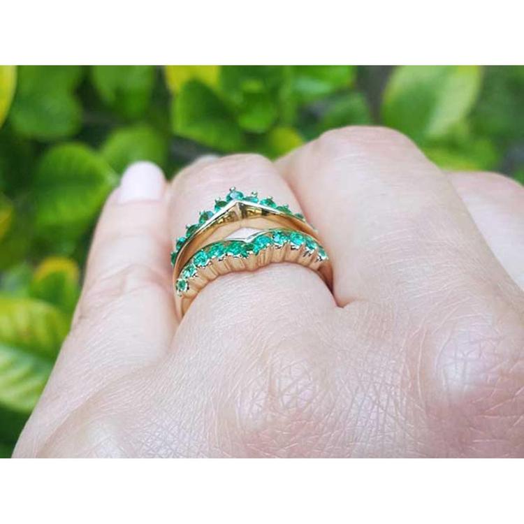 A yellow gold emerald ring guard on a hand against a blurred green leafy background,