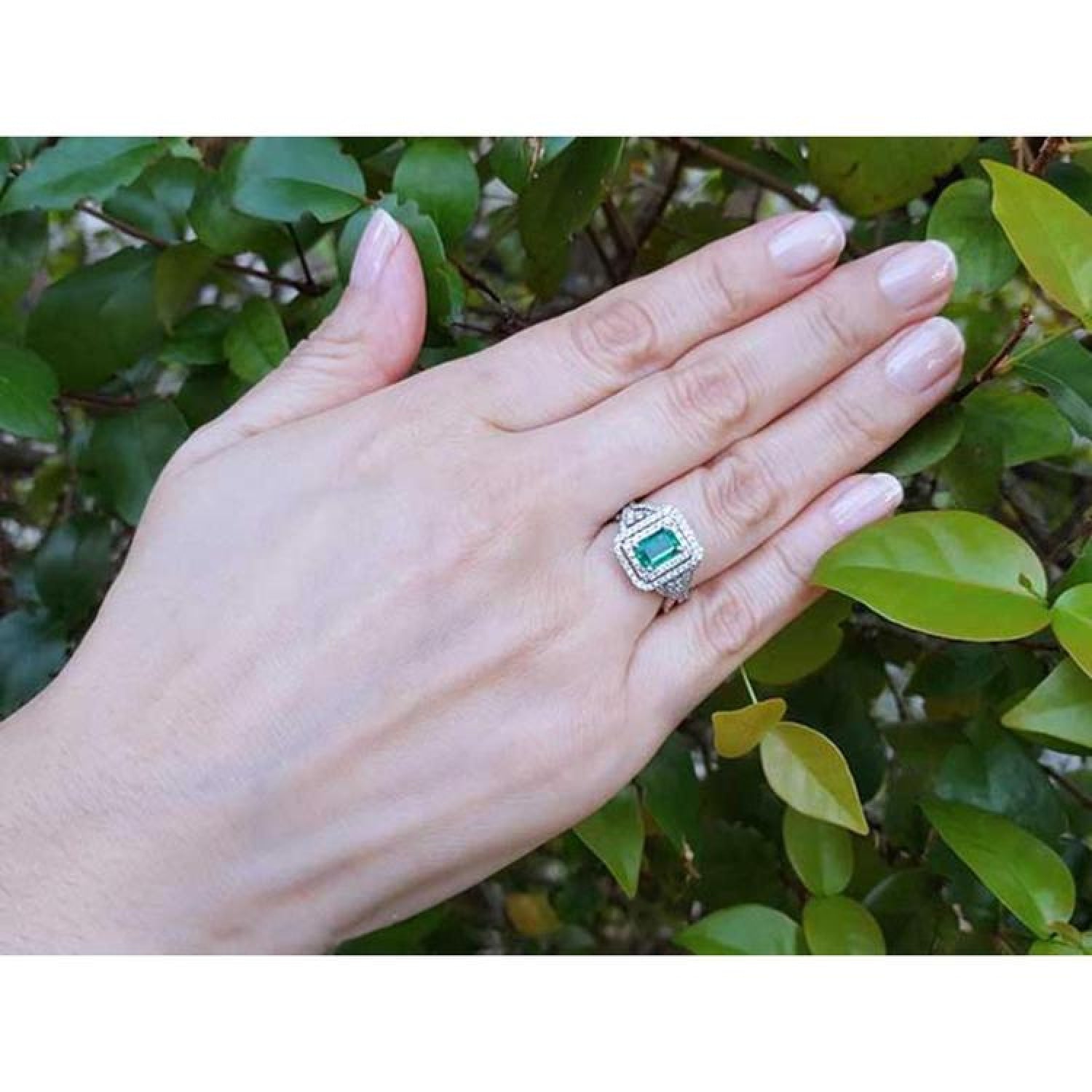 1.01 carat emerald ring with double halo diamonds and matching band in 14K white gold on a hand.