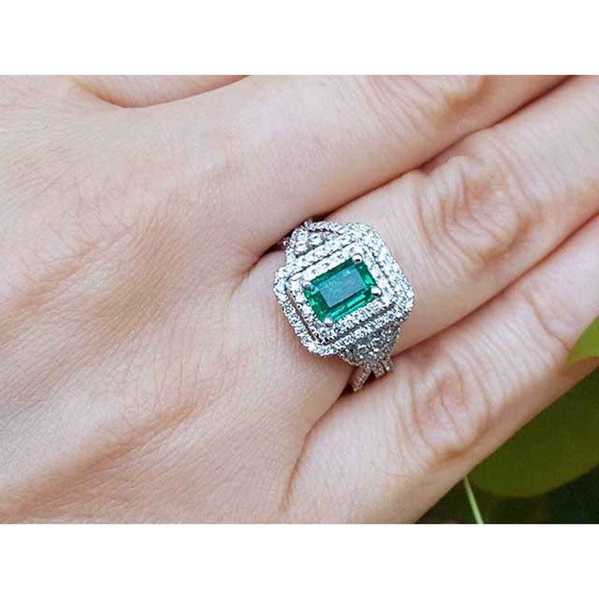 Emerald ring with double halo diamond on a hand against a natural background.