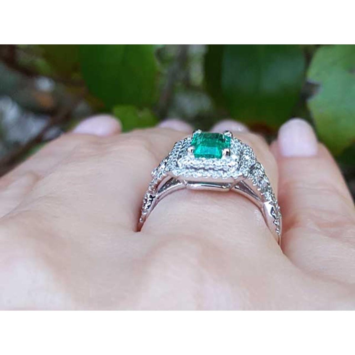 A white gold emerald ring on a hand against a blurred green background.
