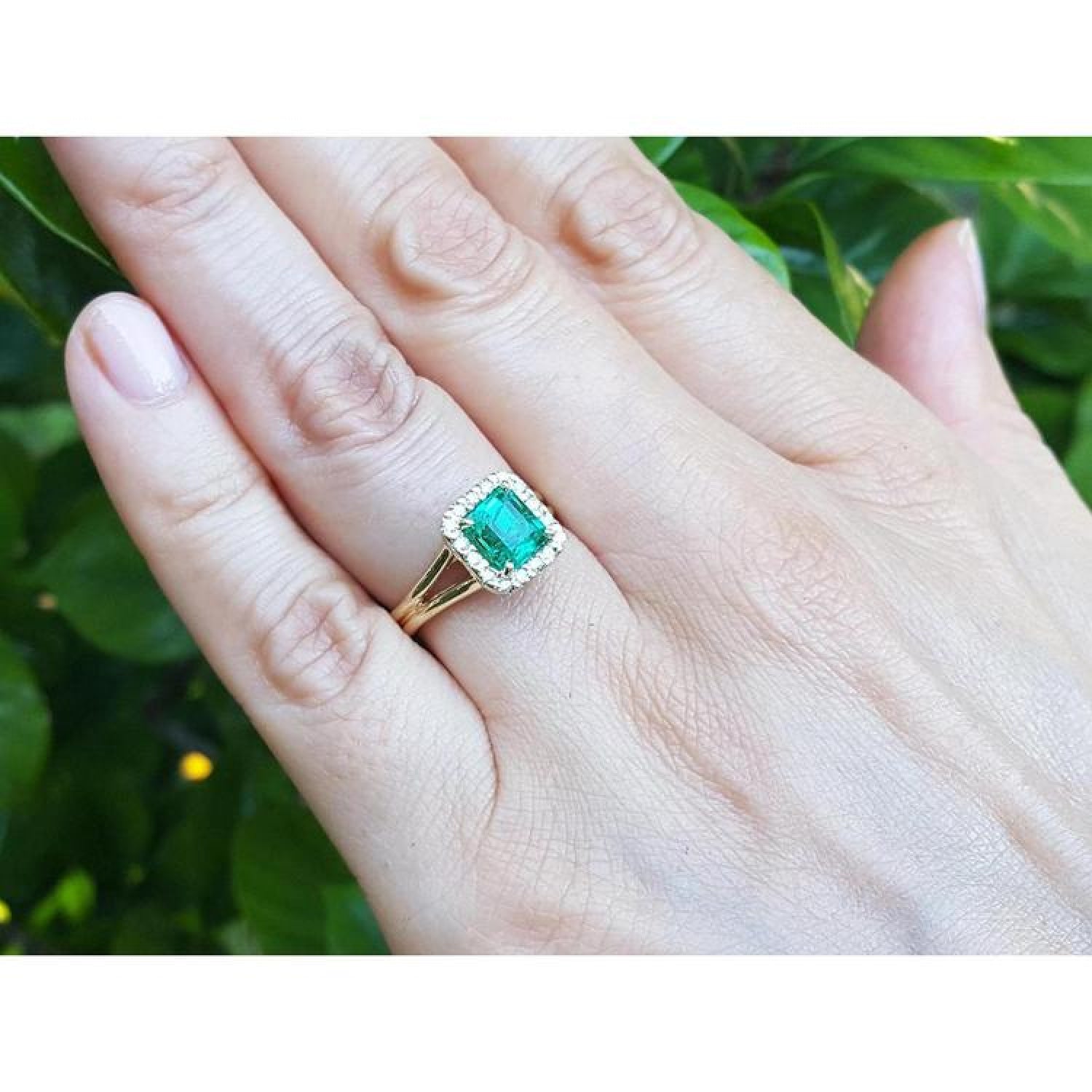 1.27 carat Colombian emerald ring with halo diamonds and split shank in 14K yellow gold on a hand.