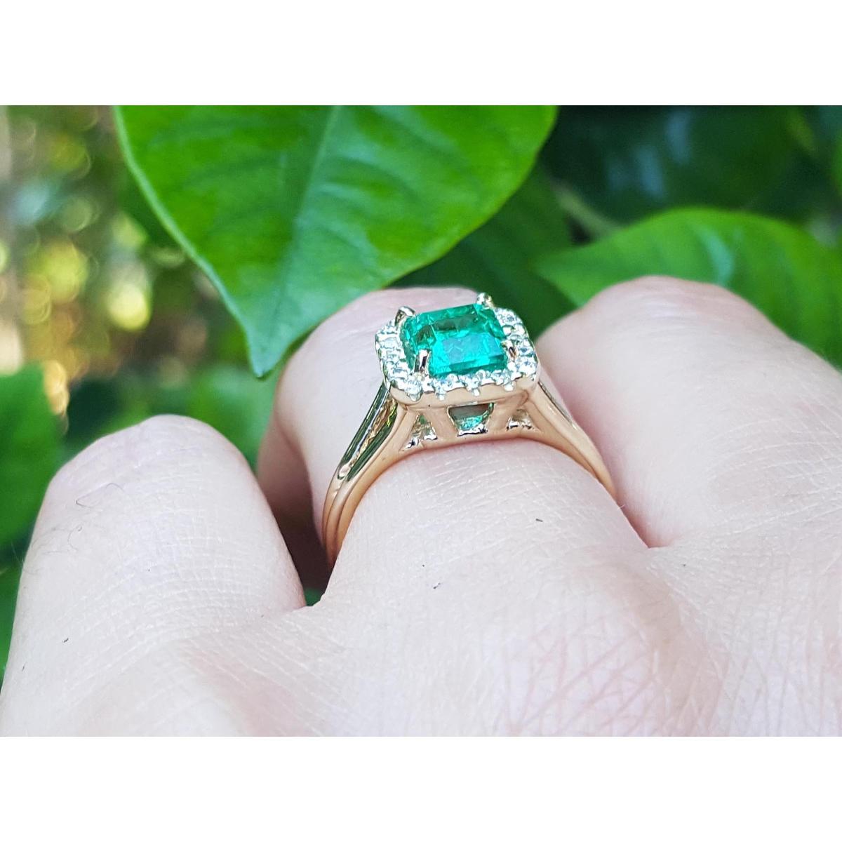 Emerald halo diamond ring underside view on a finger over green leaves background.