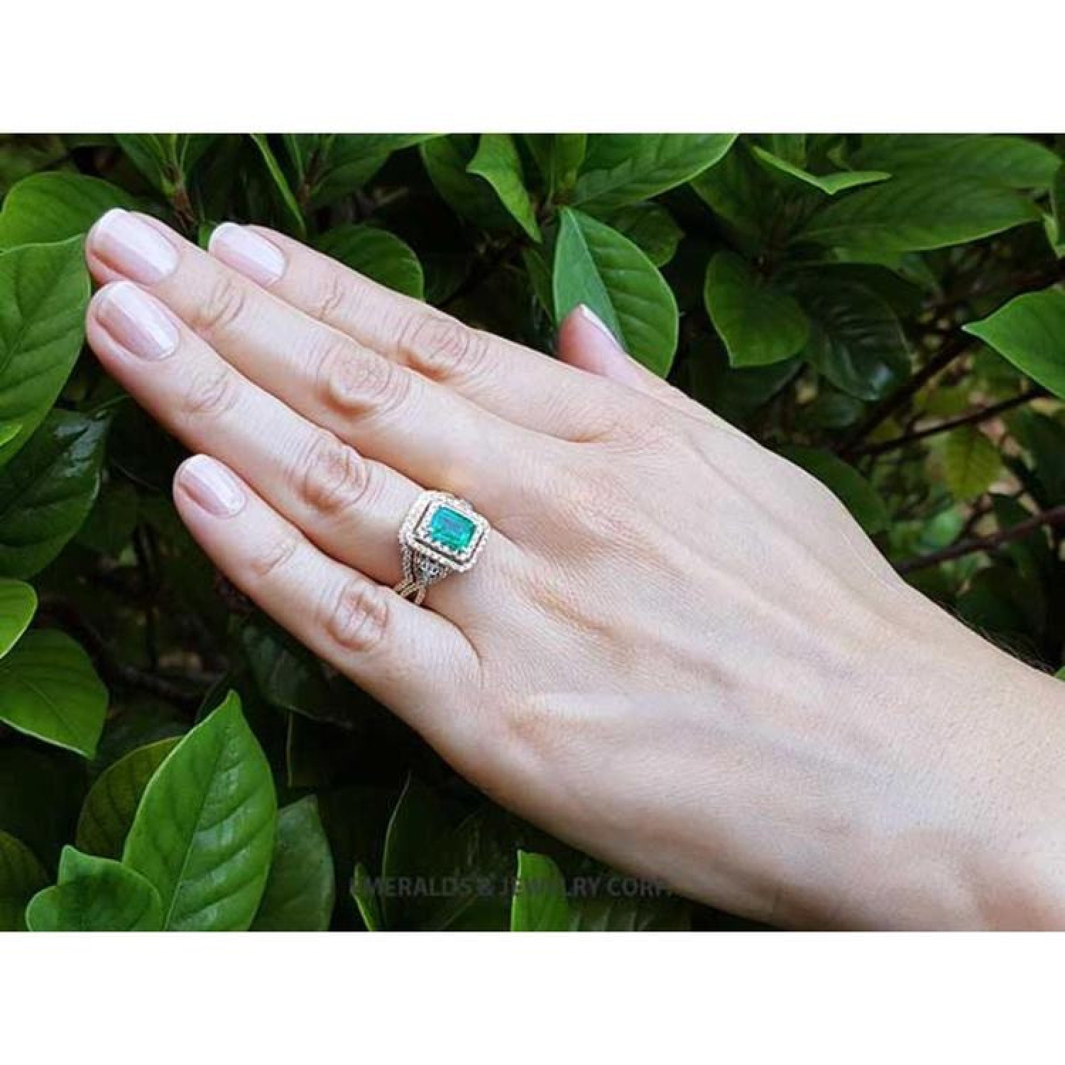 Emerald-cut emerald ring with double diamond halo and matching band in 14K yellow gold on a hand.