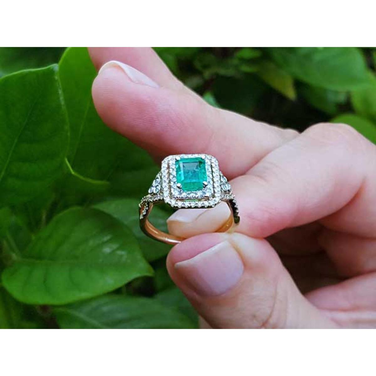 Ring with a natural colombian emerald held between fingers against a natural background.
