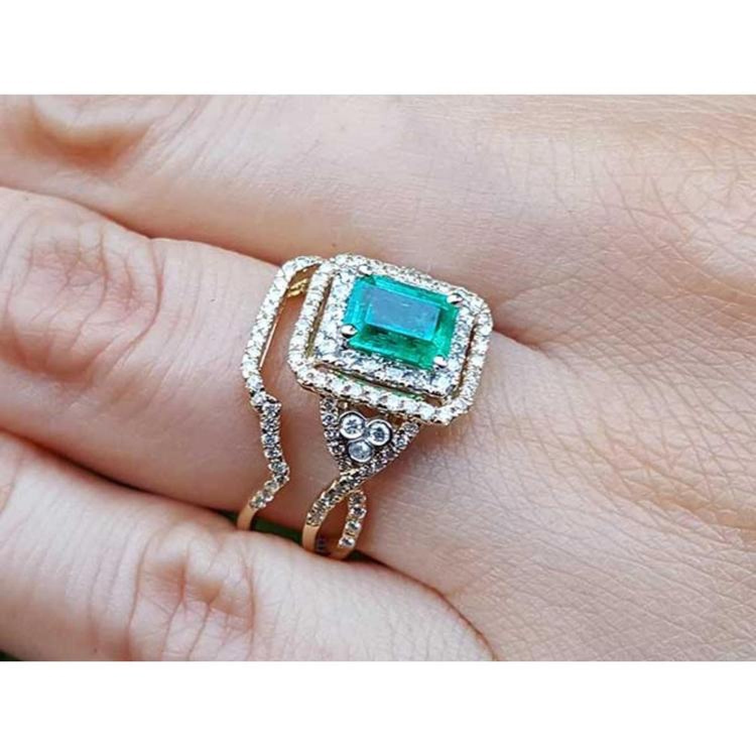 1.31 ct. emerald-cut emerald ring with double diamond halo and matching 14K yellow gold band on a finger.