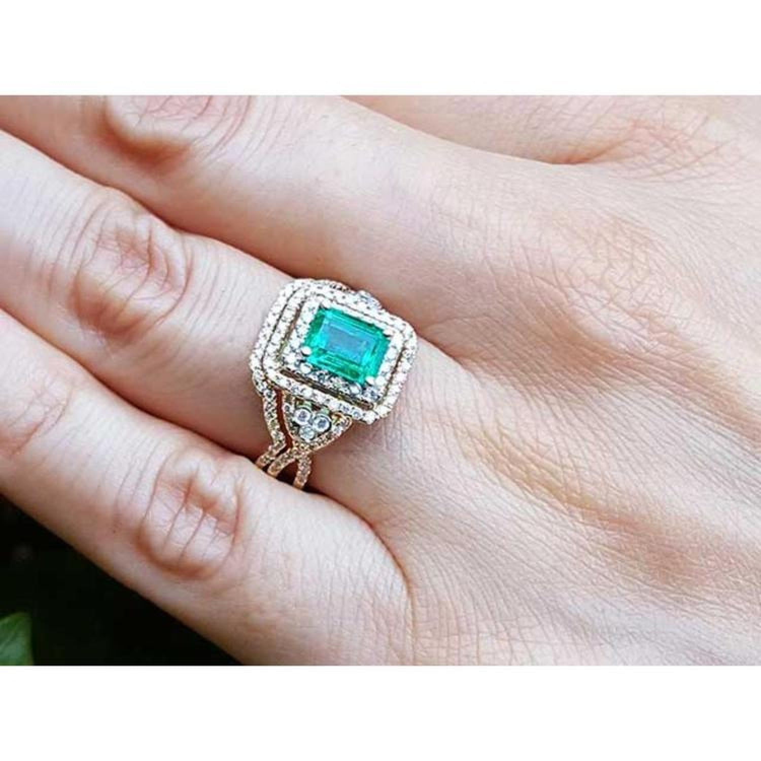 Emerald-cut emerald ring with double diamond halo and matching band in 14K yellow gold on a hand.