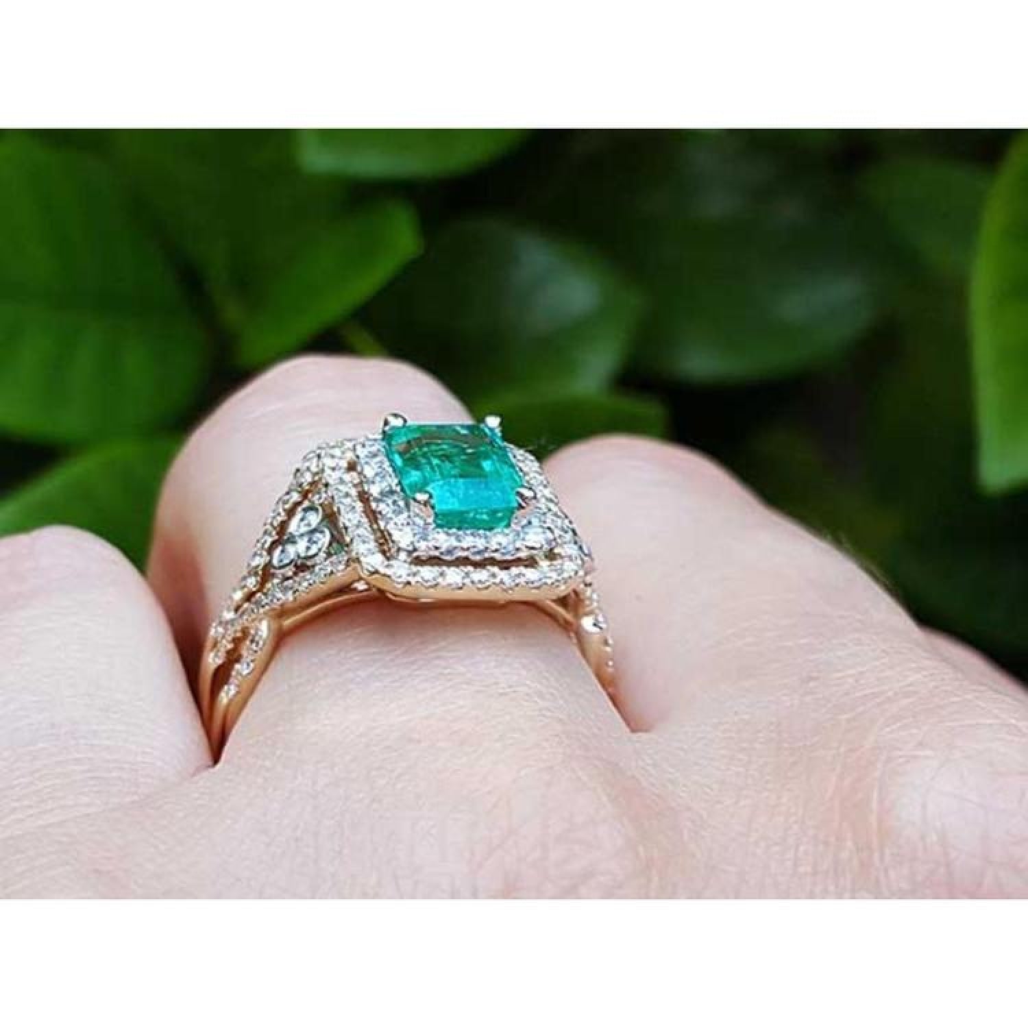 14K yellow gold emerald-cut emerald ring with double diamond halo and matching band on a finger.