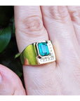 Gold ring with a natural Muzo colombian emerald on a finger against a blurred natural background.