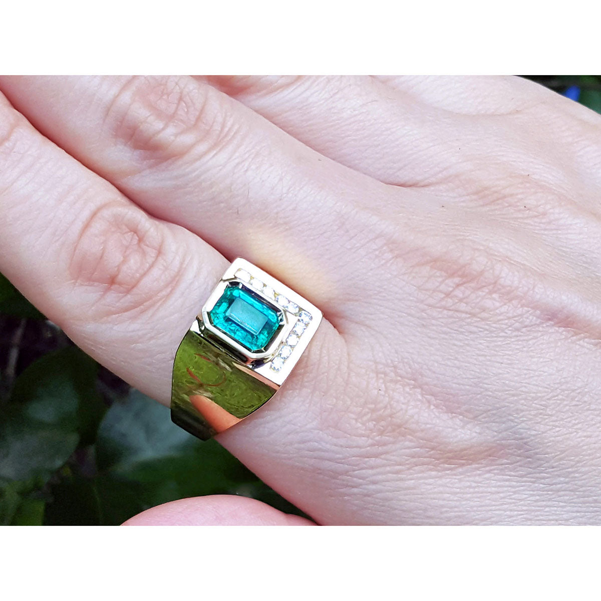 A mens emerald ring in yellow gold being worn on a finger.