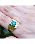 A mens emerald ring in yellow gold being worn on a finger.