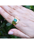 Gold ring for men with a colombian emerald on a hand against a green leafy background.
