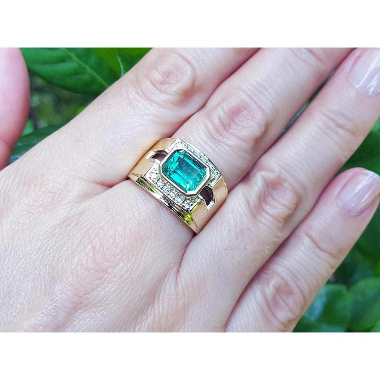 Gold mens ring with a natural colombian emerald on a hand against a green leafy background