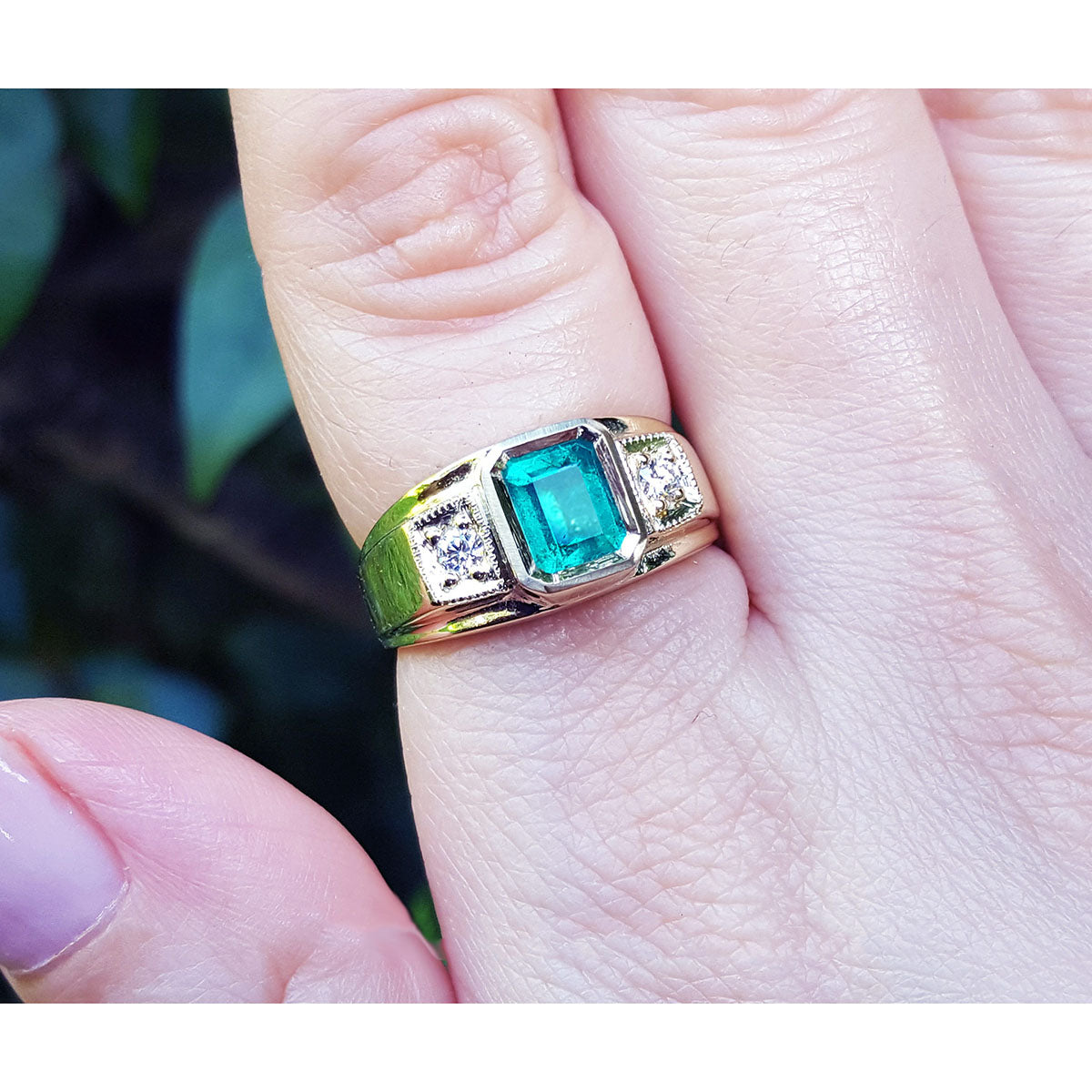 Gold ring for man with a natural colombian emerald on a finger against a blurred natural background.